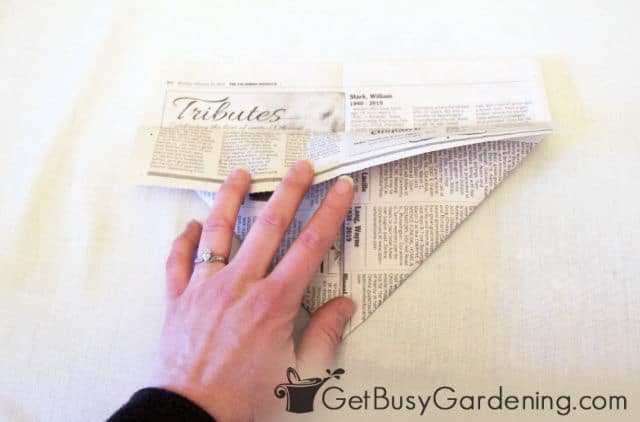 Folding the top edge of the newspaper over the triangles