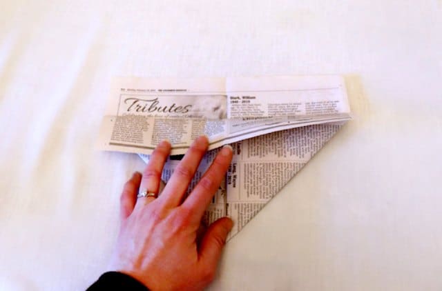 Folding the top edge of the newspaper over the triangles Folding the top edge of the newspaper over the triangles