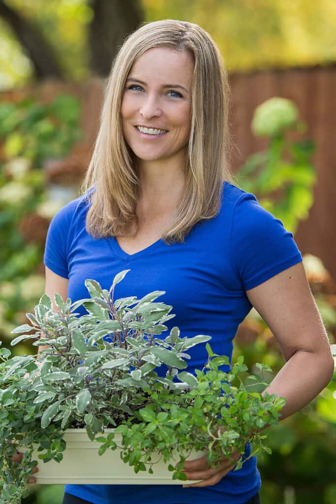 Amy Andrychowicz standing in her garden holding a container of herbs
